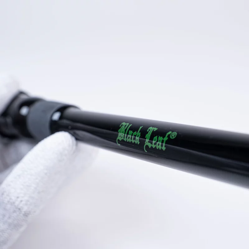 Hand in weißen Handschuhen hält Chillum aus Glas, schwarz, mit grünem Black Leaf Schriftzug und sichtbarem Schliff im Mittelteil