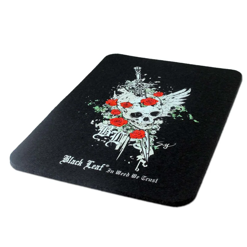 Rechteckige schwarze Matte aus Gummi mit aufgedrucktem Motiv, weißer Totenschädel mit Flügel und Schwert, darauf verteilt rote Rosen, dazu das Black Leaf Logo und der Spruch 'In Weed We Trust'
