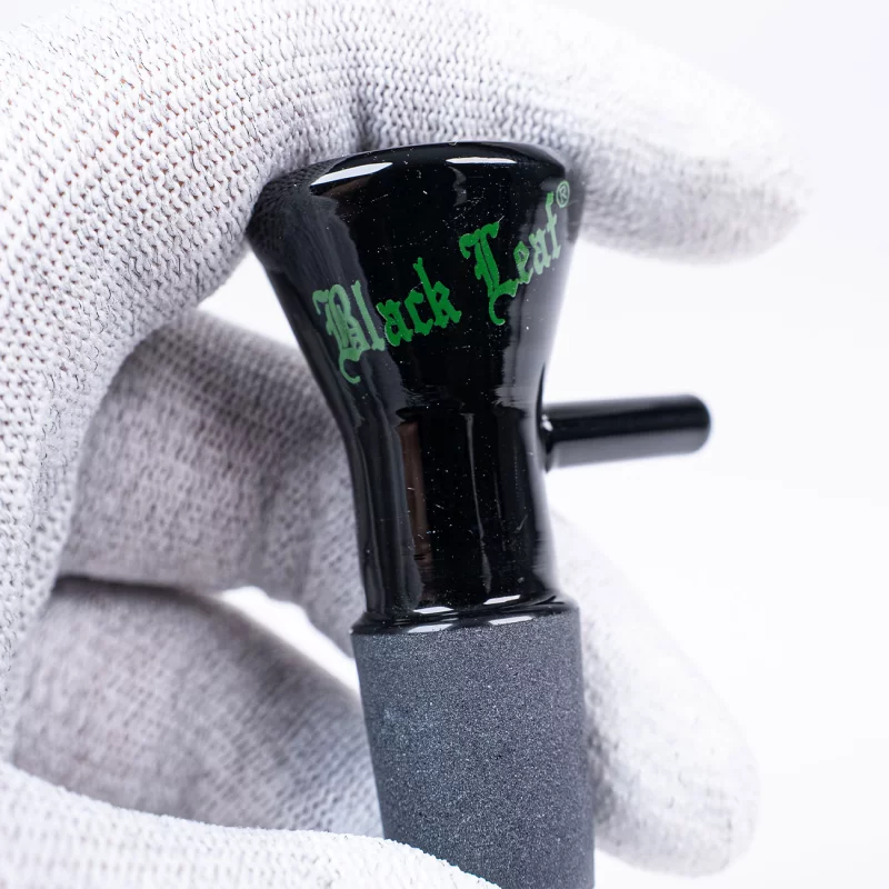 Bong-Kopf aus Glas, schwarz mit grünem Black Leaf Logo, trichterförmig mit Rollstopp und Lift-off-Griff an der Seite, wird von Hand in weißem Handschuh gehalten
