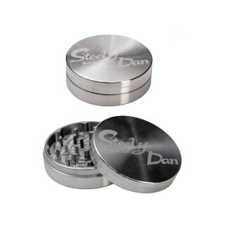 Grinder aus Metall, zylindrische Form, silberfarben. Oberes Teil mit Schriftzug Steely Dan graviert. Unteres Teil geöffnet, zeigt Zahnstrukturen. TÜV-Siegel oben rechts im Bild.